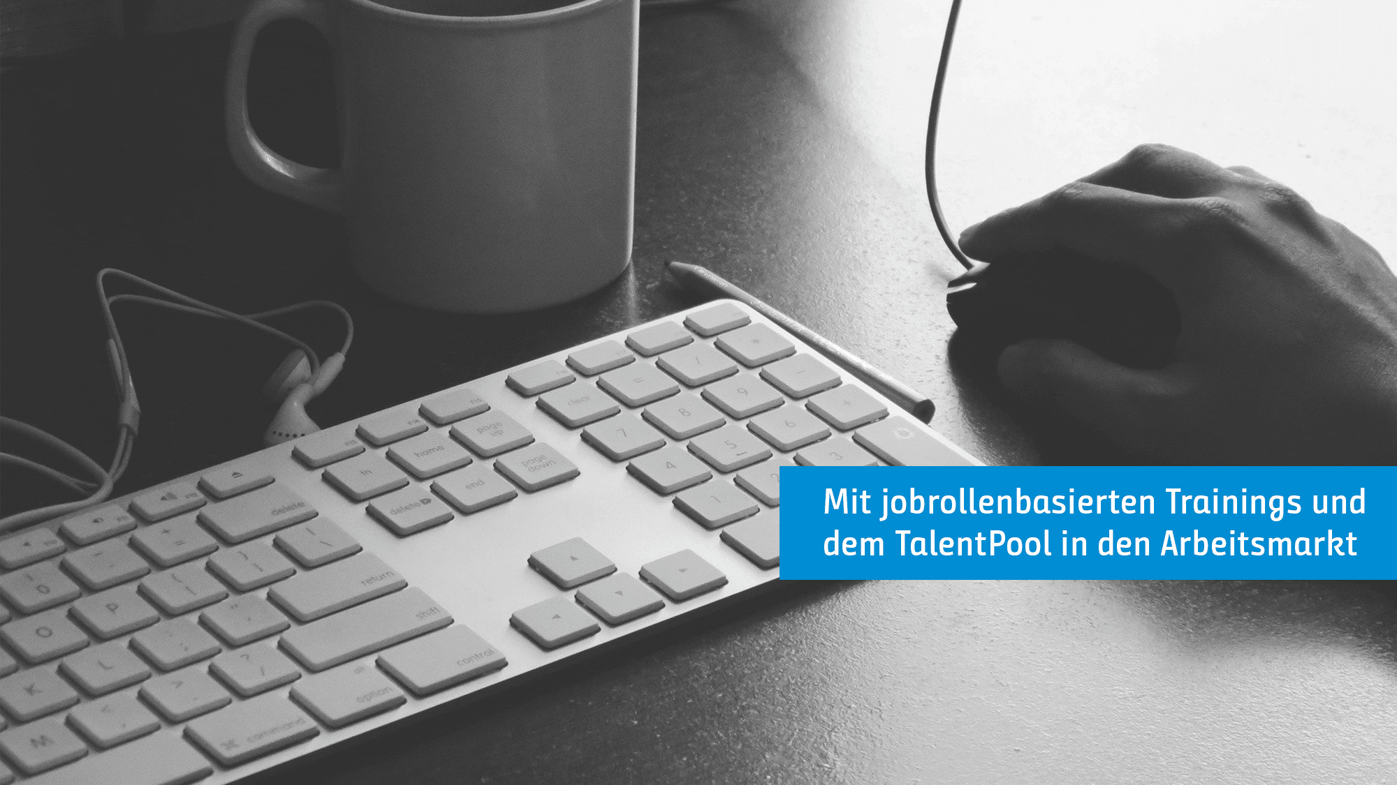 Eine Nahaufnahme der Hand einer Person, die eine Computermaus benutzt. In der Nähe befindet sich eine Tastatur und eine Kaffeetasse. Es gibt eine blaue Überlagerung mit weißem Text auf Deutsch: „Mit jobrollenbasierten Trainings und dem TalentPool in den Arbeitsmarkt.“